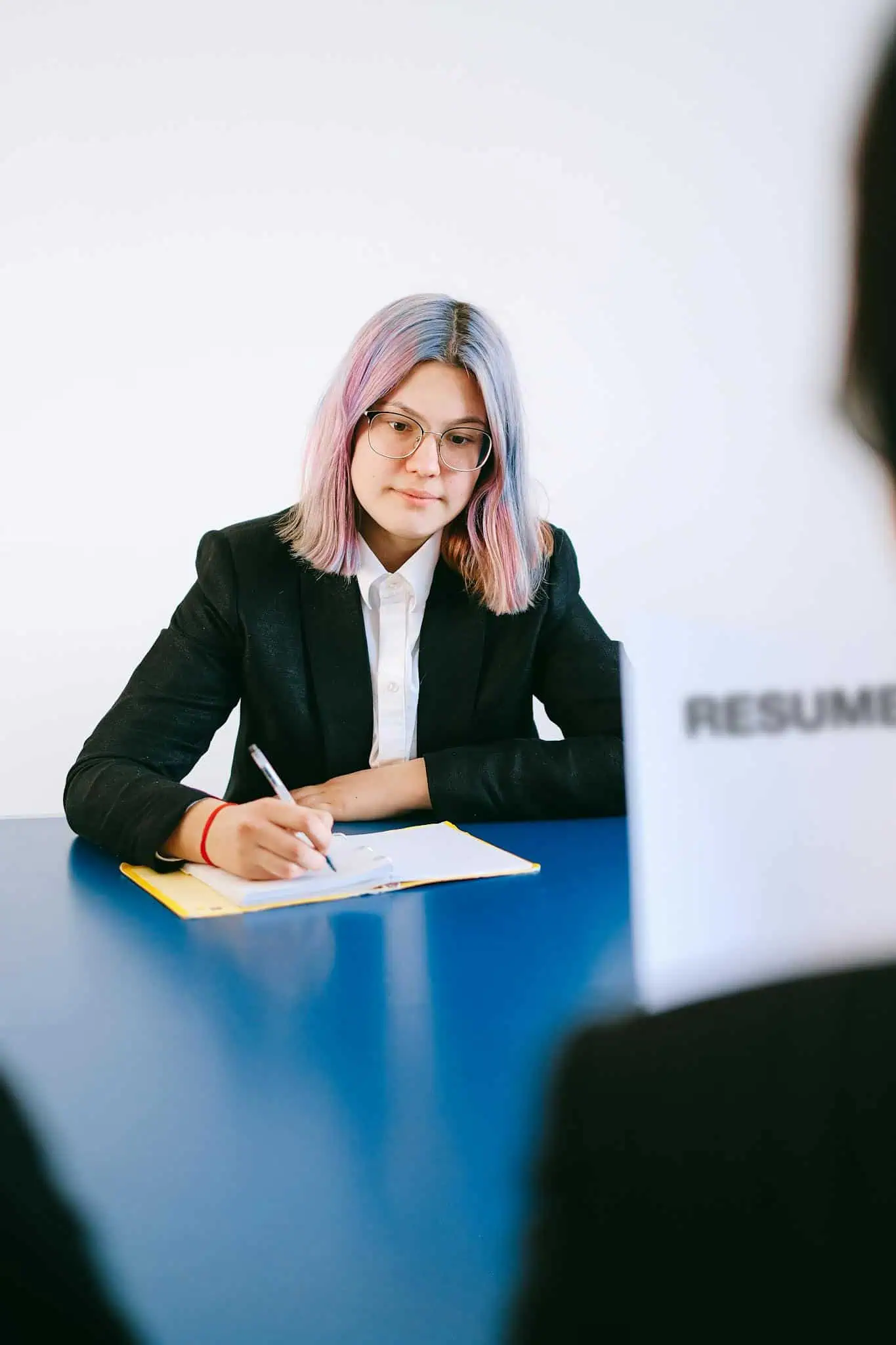 Professional woman with dyed hair taking notes during a job interview.
